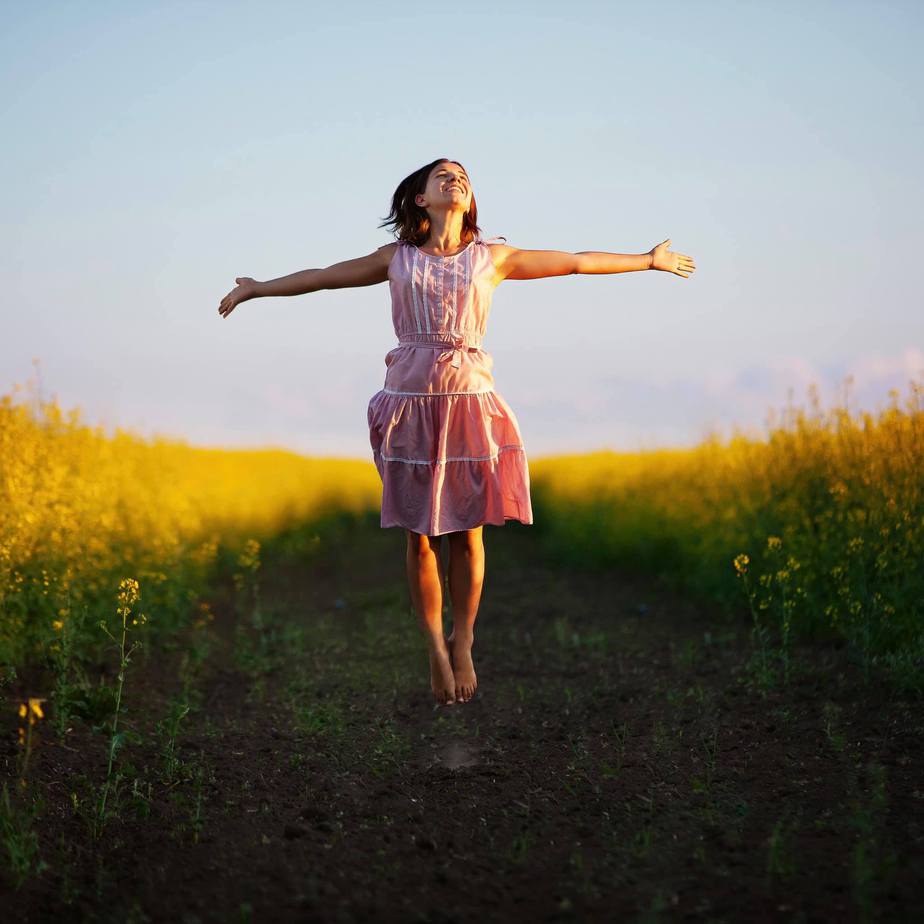 eosKgVm2P5E5HeVy2UEV.png A girl is jumping in a field with her arms outstretched.