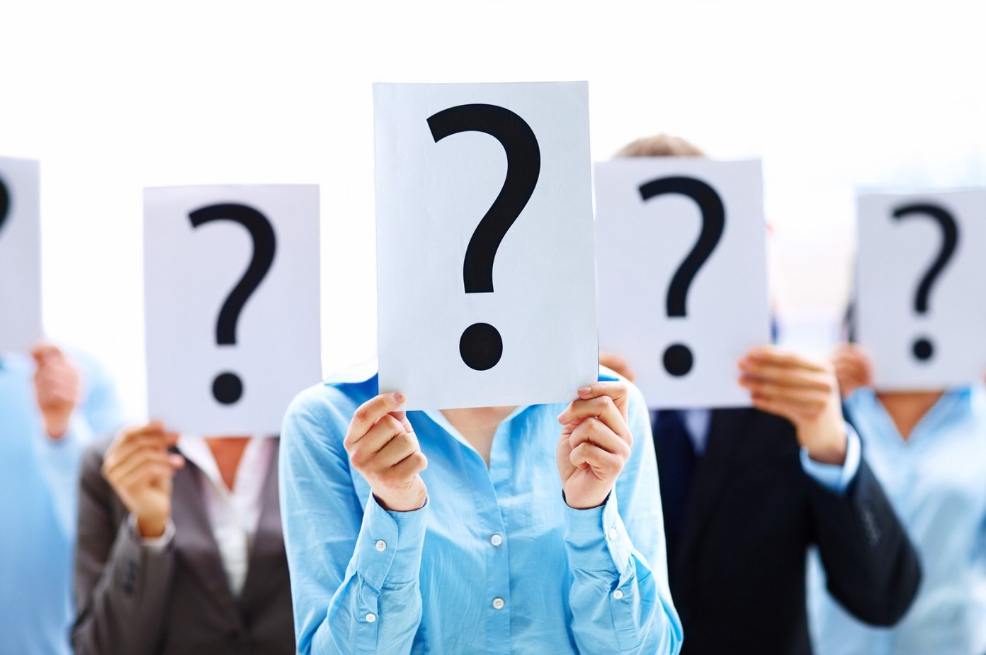 Five people stand in a row, each holding a sheet of paper with a large black question mark in front of their face, obscuring their identity.