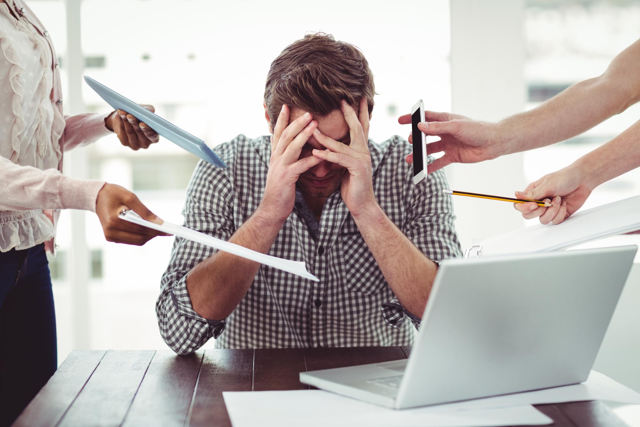 3 powerful tips to manage stress A man is holding his head in front of a group of people.